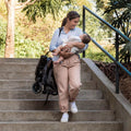 Woman carrying a baby and a backpack while walking up stairs outdoors