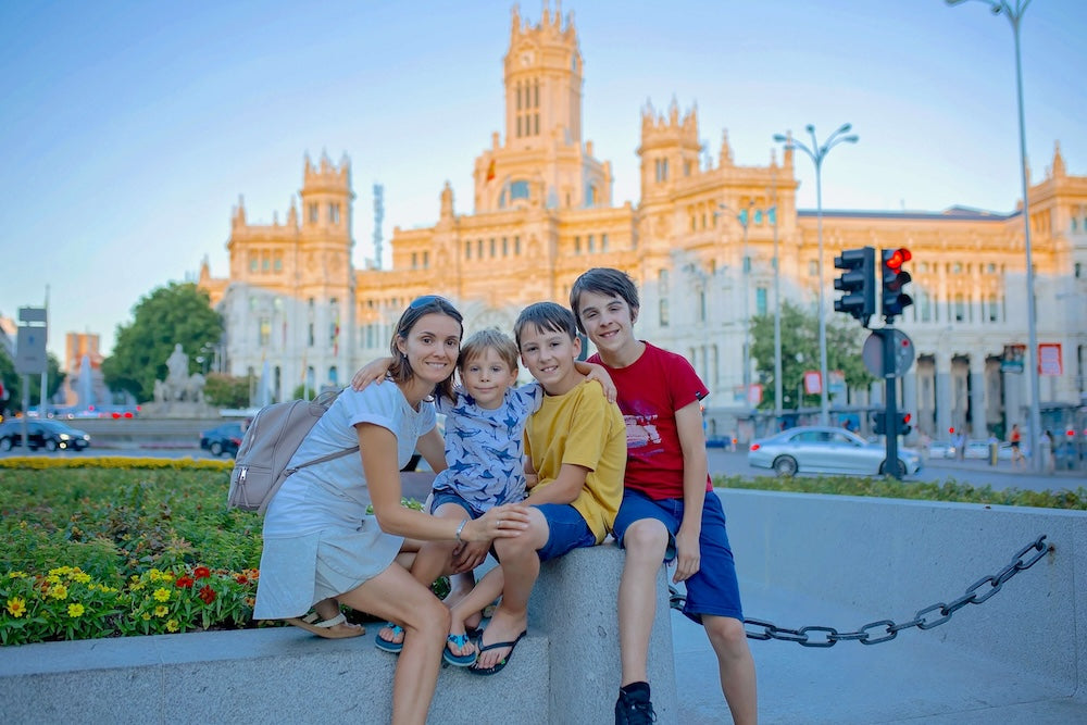 Family of four in front of a famous Madrid large, ornate building with a blue sky.