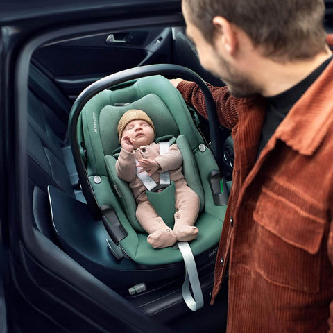 Man adjusting a green baby car seat with a baby inside in a vehicle.