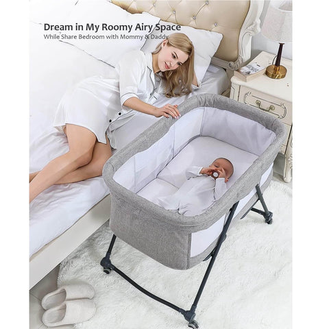 Woman lying in bed with a baby in a gray bassinet, bedroom setting.