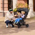 Man pushing a double stroller with two children on a brick path.