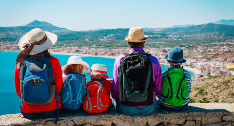 A happy family of tourists sitting together on a scenic overlook in Spain, enjoying their trip with rented baby and family gear from Equiply.